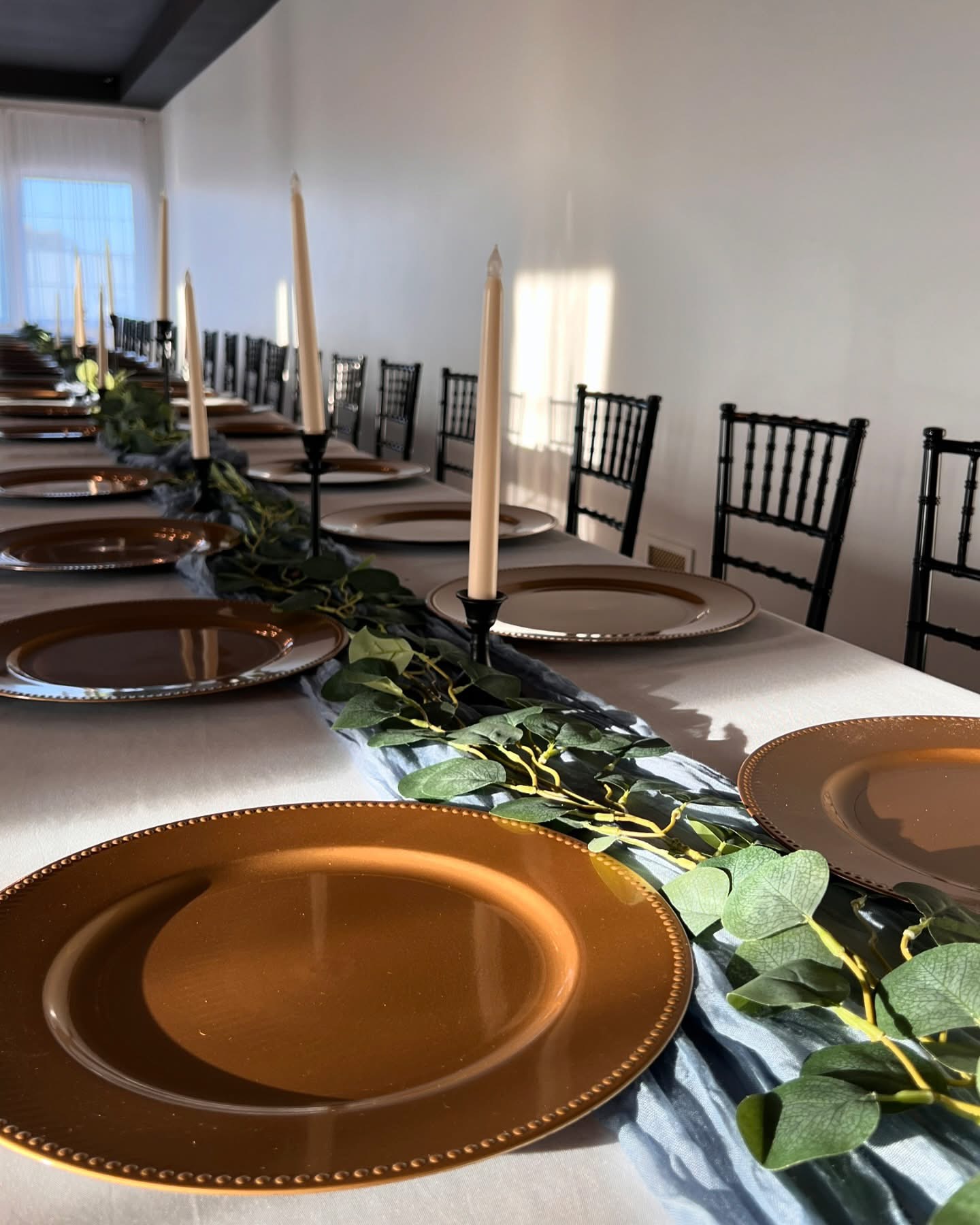 Family style table with gold chargers, eucalyptus runner and taper candles at Haley Station